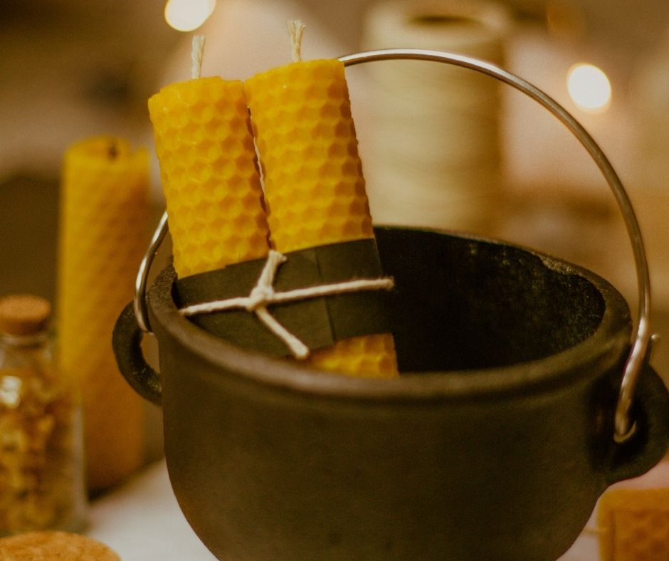 black cast iron cauldron holding two rolled beeswax pillar candles secured with black paper and twine, with more candles and rolls of twine in the background