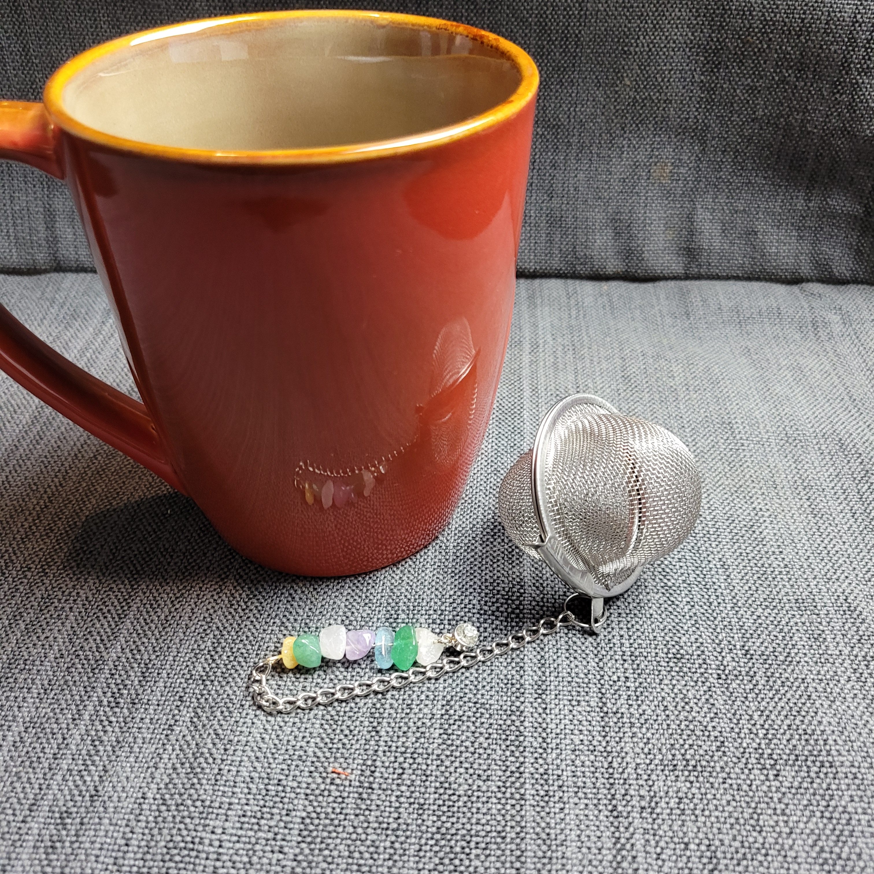 stainless steel mesh tea ball adorned with crystal chips rests casually in front of a large tea mug